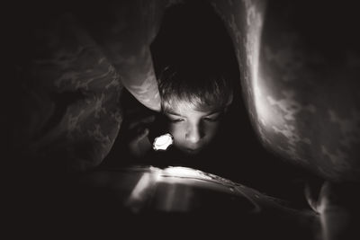 Boy reading book using flashlight in darkroom