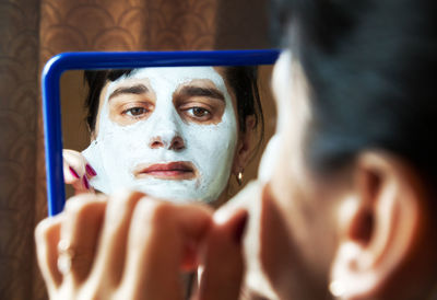 Reflection of woman removing facial mask in mirror at home