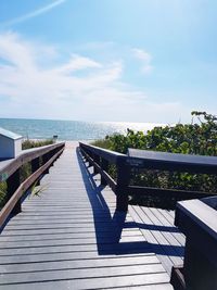 Empty wooden walkway by sea against sky