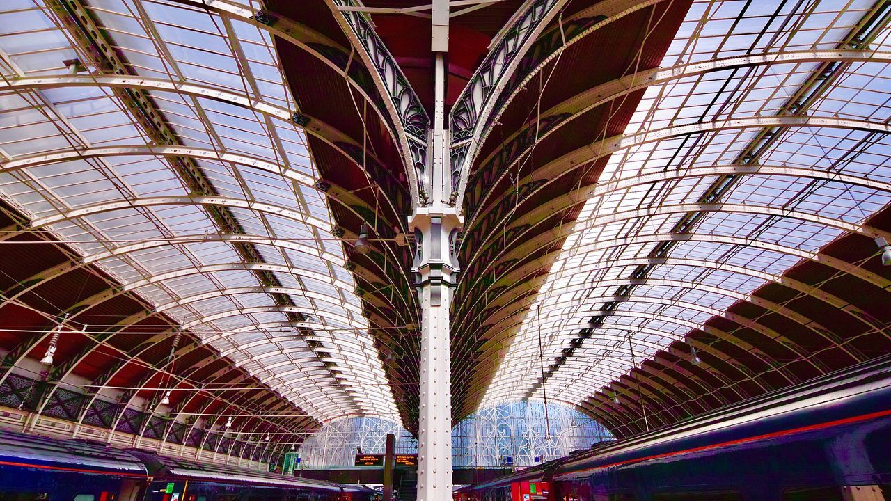 ceiling, transportation, architecture, built structure, indoors, incidental people, arch, mode of transportation, rail transportation, public transportation, travel, railroad station, lighting equipment, illuminated, modern, low angle view, train, pattern, city, architectural column, subway train