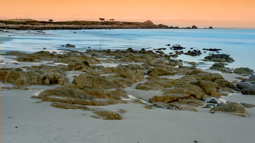 Rocks on beach against sky during sunset