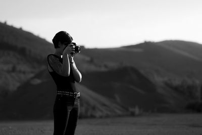 Woman photographing with digital camera while standing against mountains