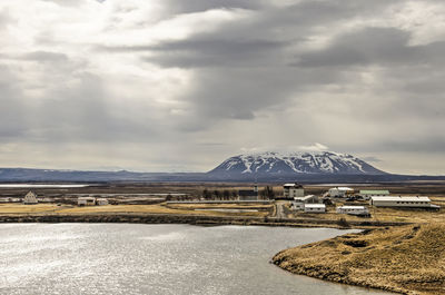 View of the small village by the lake with a distant snow-capped mountain under a dramatic sky