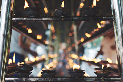 Close-up of illuminated diyas on railing at temple