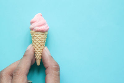 Cropped hand of person holding of ice cream cone against blue background