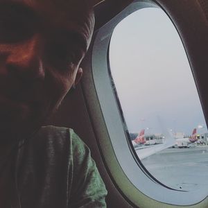 Close-up of man looking through airplane window