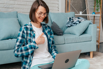 Young woman using mobile phone while sitting on sofa at home