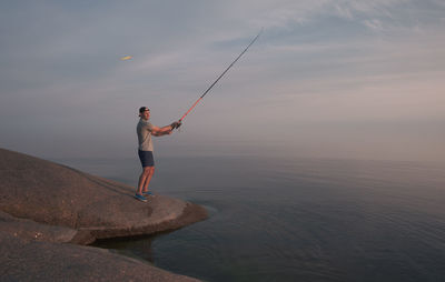 Rear view of man standing on rock by sea against sky