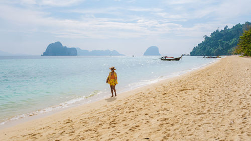 Rear view of woman standing at beach against sky