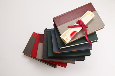 Close-up of diploma on stacked books against white background