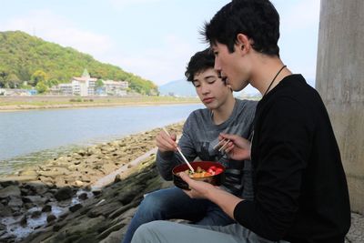 Young men eating at riverside