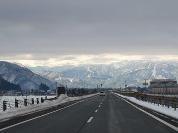 Road by snowcapped mountains against sky