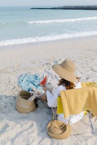 Woman with coconut and slice of watermelon sitting on chair at beach