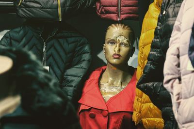 Old weathered mannequin wearing red jacket by winter coats in store