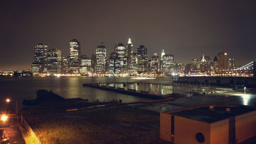 Illuminated buildings by river against sky at night