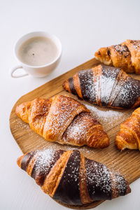 Bunch of appetizing brown and chocolate croissants with powdered sugar on a wooden board