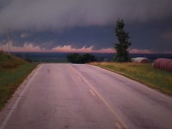 Empty country road against cloudy sky