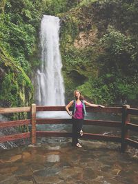 Woman standing on footbridge against waterfall