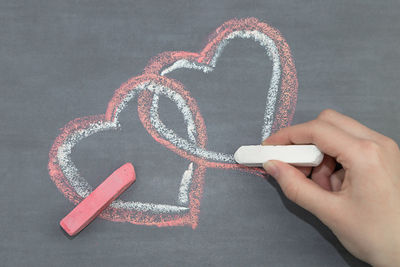 Cropped hand of woman drawing heart shape on blackboard