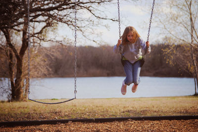 Girl swinging at lakeshore against sky