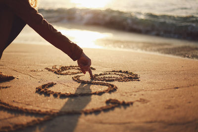 Midsection of mid adult woman writing on sand at beach