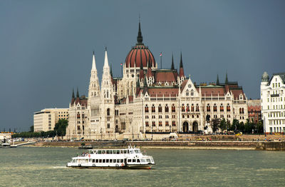 Boat on river by buildings against sky in city