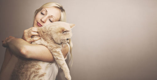 Beautiful woman holding cat against beige background