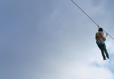 Low angle view of woman hanging on rope against sky