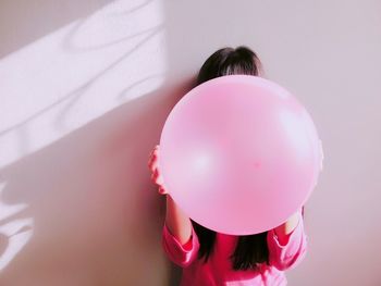 Woman holding pink balloon standing against wall