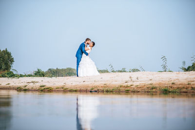 Woman standing on riverbank against clear blue sky