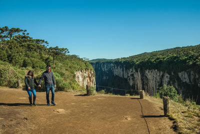 Rear view of people walking on mountain against clear blue sky