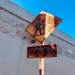 Close-up of rusty sign against blue sky