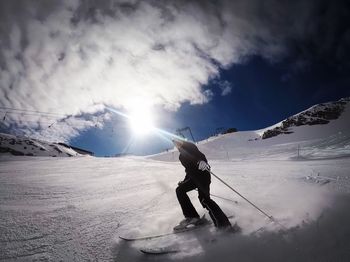 Low angle view of young woman skiing on snow covered field against cloudy sky