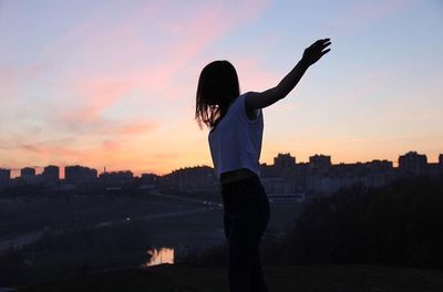 Woman with arms outstretched against sunset sky