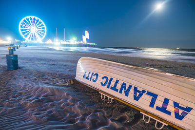 Illuminated text on beach against sky at night