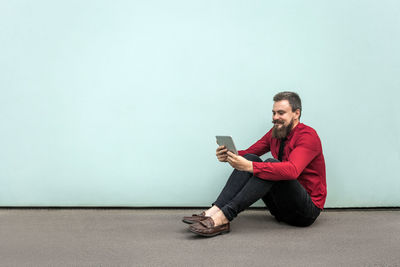 Young man using mobile phone while sitting on wall