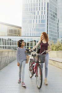 Mother and daughter walking with bicycle on footbridge in city