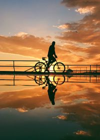 Silhouette man bicycle on bridge against sky during sunset