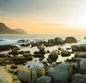 Rocks on beach against sky during sunset