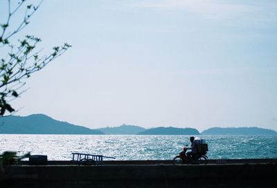 People riding motorcycle on sea against clear sky