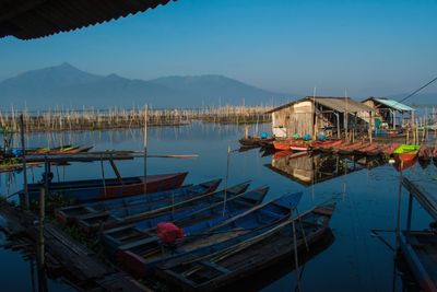 Boats moored in harbor by houses against sky