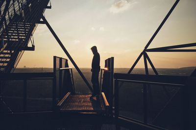 Silhouette person standing on metal grate against sky during sunset