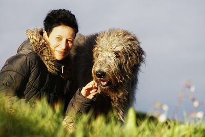 Portrait of woman with irish wolfhound sitting on field against sky