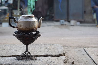 Close-up of teapot over charcoal on footpath