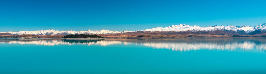 Scenic view of lake by snowcapped mountains against blue sky