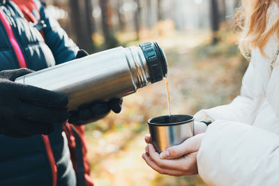 Women having break during autumn trip pouring a hot drink from thermos flask on autumn cold day