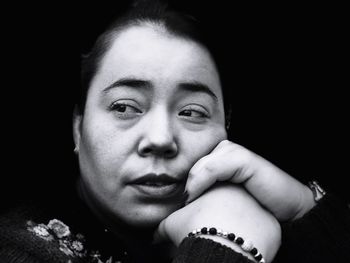 Close-up of thoughtful mid adult woman against black background