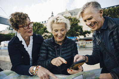 Senior male and female friends with map and mobile phone in city