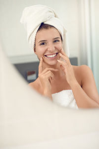Reflection of smiling young woman applying moisturizer on face in mirror
