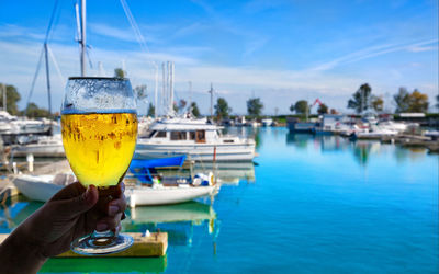 Hand holding drink by swimming pool against blue sky